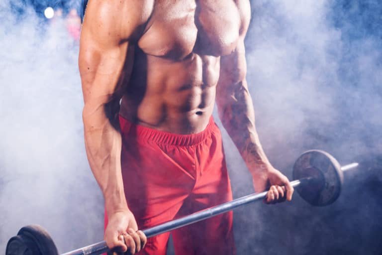Powerful bodybuilder doing the exercises with barbell. Photo of strong male with naked torso on dark background. Strength and motivation.