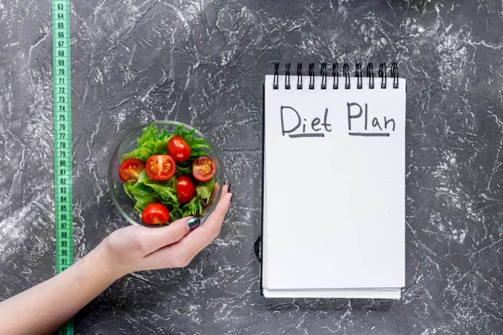 The Satiating Diet: Are You Prepared For A Good Thing? 2 notebook-for-diet-plan-salad-and-measuring-tape-on-grey-stone-table-top-view