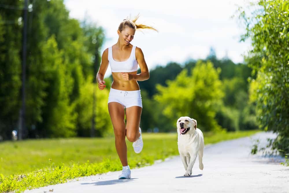 Young attractive sport girl running with dog in park