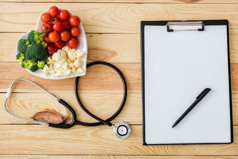 Top view of blank clipboard with pen near stethoscope and tasty vegetables on heart-shape plate