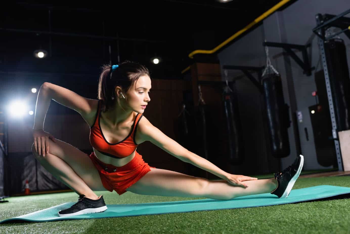 The Why, When, and How of Stretching 1 Sportswoman in top and shorts stretching legs on fitness mat in sports center