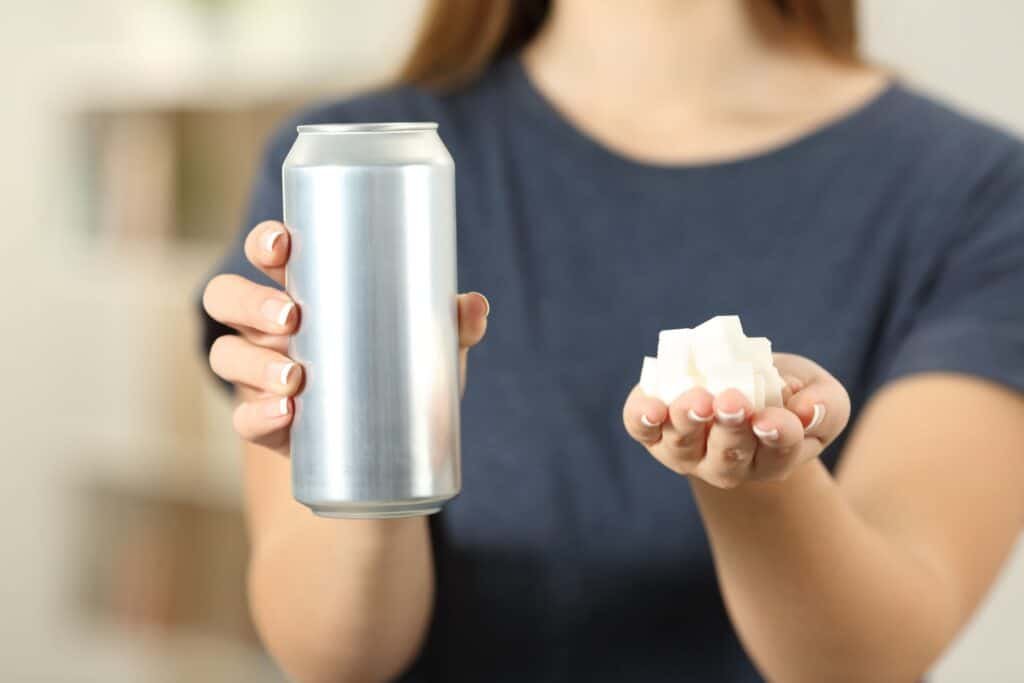 10 Surprisingly Easy Weight Loss Hacks You Need to Try Today 3 Front view close up of a woman hands holding a soda drink and sugar cubes.