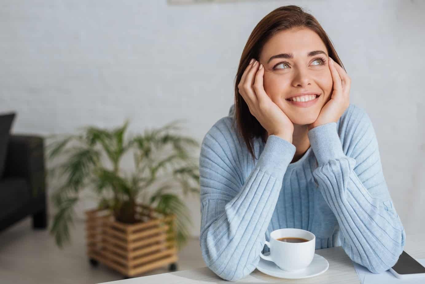 From Negative to Positive: Discover the 10 Benefits of Positive Thinking 1 Dreamy young woman smiling near cup with coffe