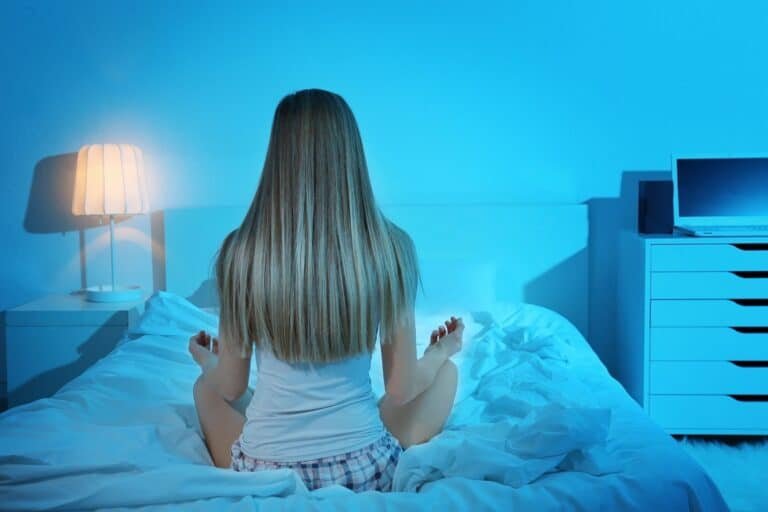Beautiful young woman meditating while sitting on bed at home