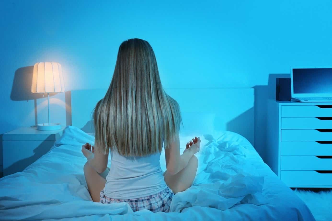 Sleep Meditation for Anxiety- A Quick Relief Guide 1 Beautiful young woman meditating while sitting on bed at home