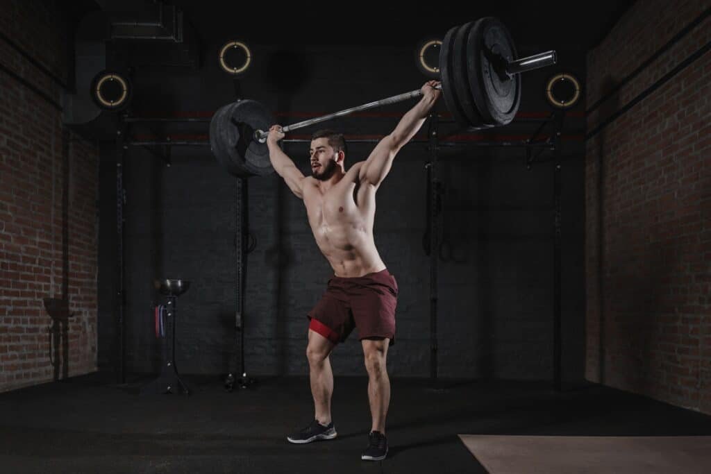 The Benefits of CrossFit: Unlocking Optimal Fitness and Health 4 Crossfit athlete lifting barbell overhead at the gym.