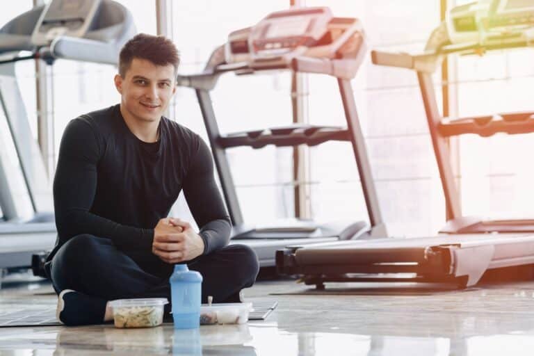 Stylish guy in the gym relaxing on the floor and eating healthy food