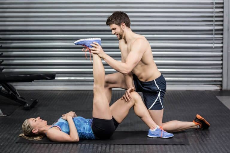Benefits Of Assisted Stretching:Male trainer assisting woman stretching