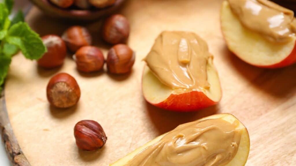 Fuel Your Gains: 10 Nutritious Snacks for Bodybuilders 9 Wooden Board of Tasty Apple Wedges with Nut Butter and Hazelnuts, Closeup
