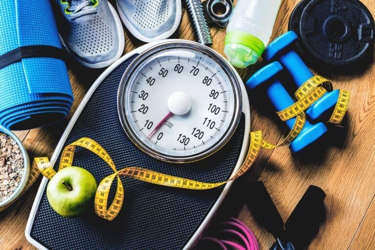 Sports and workout equipment on a wooden floor with healthy snack and weight loss scale